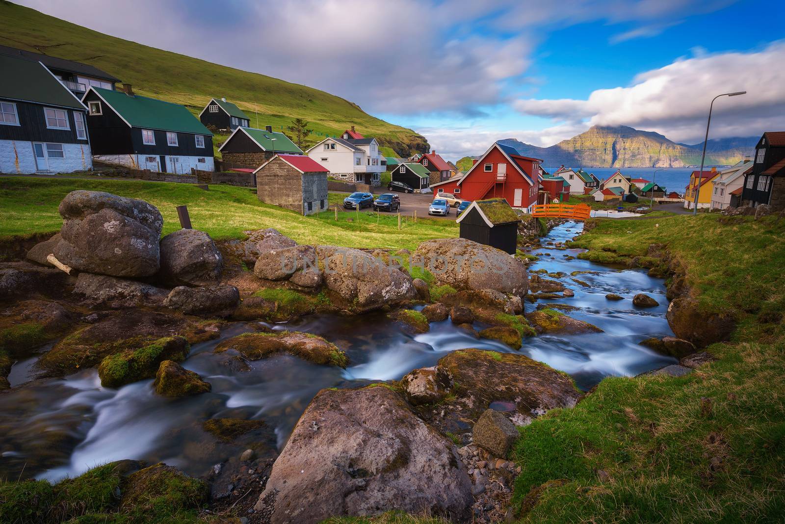 Village of Gjogv on Faroe Islands with colourful houses and a creek, with views of Kalsoy island located across the fjord. Long exposure.