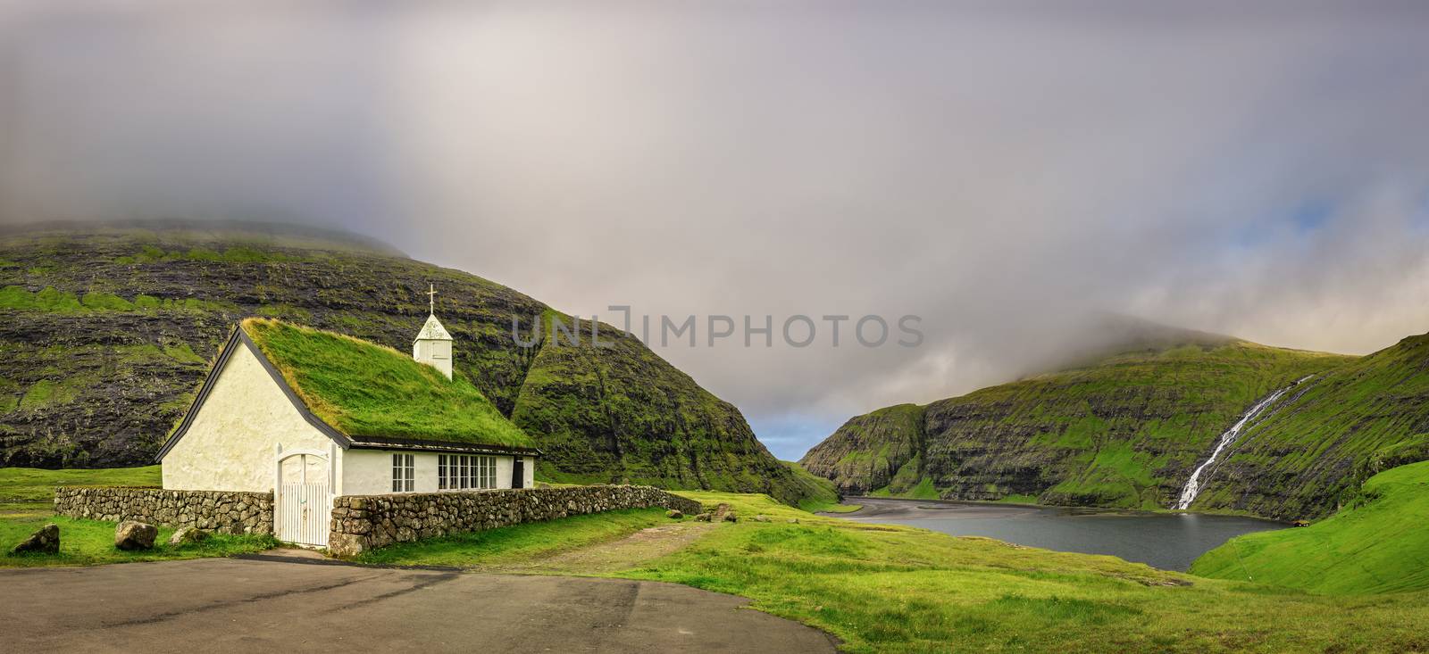Panorama of a small village church in Saksun, nearby lake and a waterfall located on the island of Streymoy, Faroe Islands, Denmark