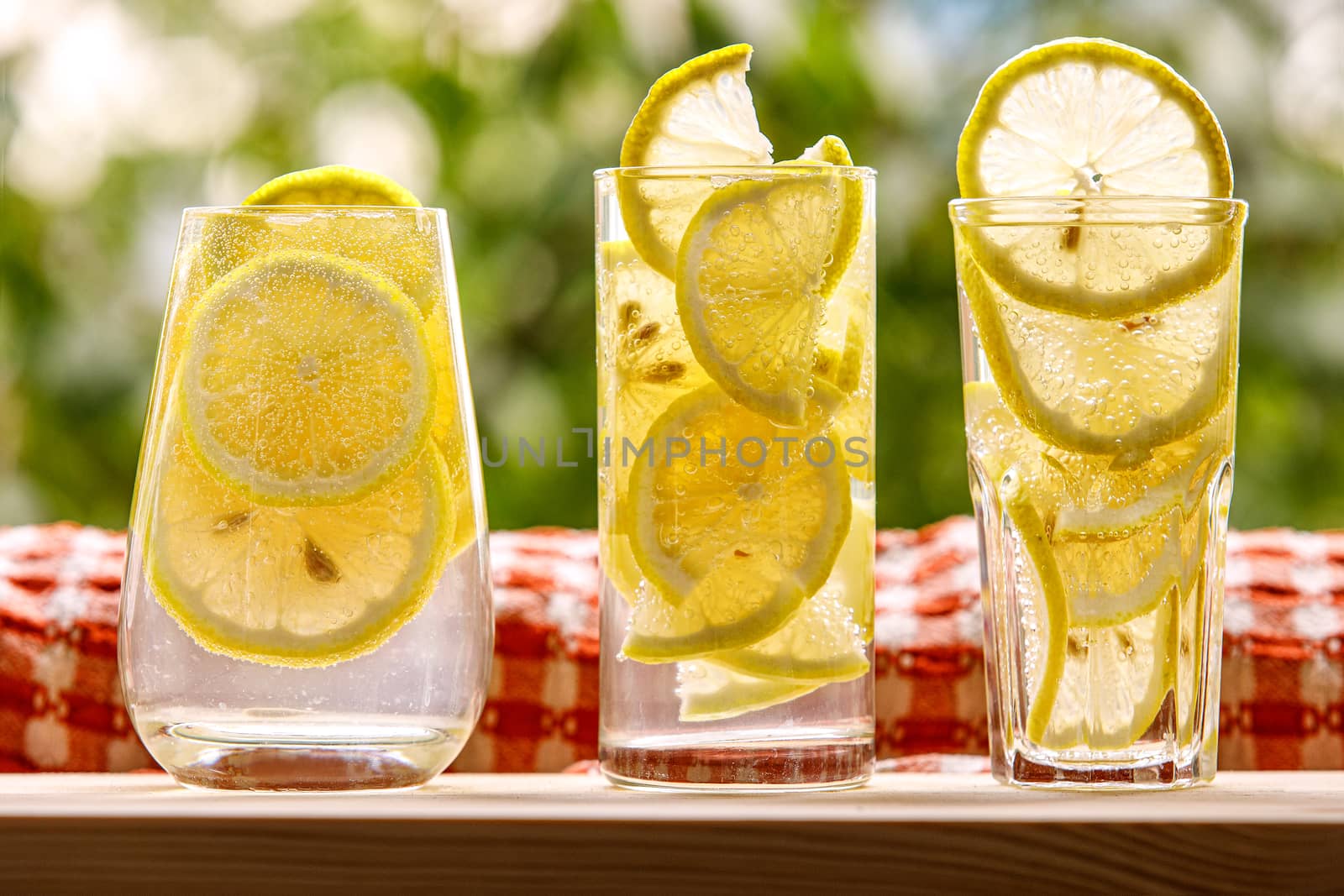 Three glasses of lemon water on the sunny garden background