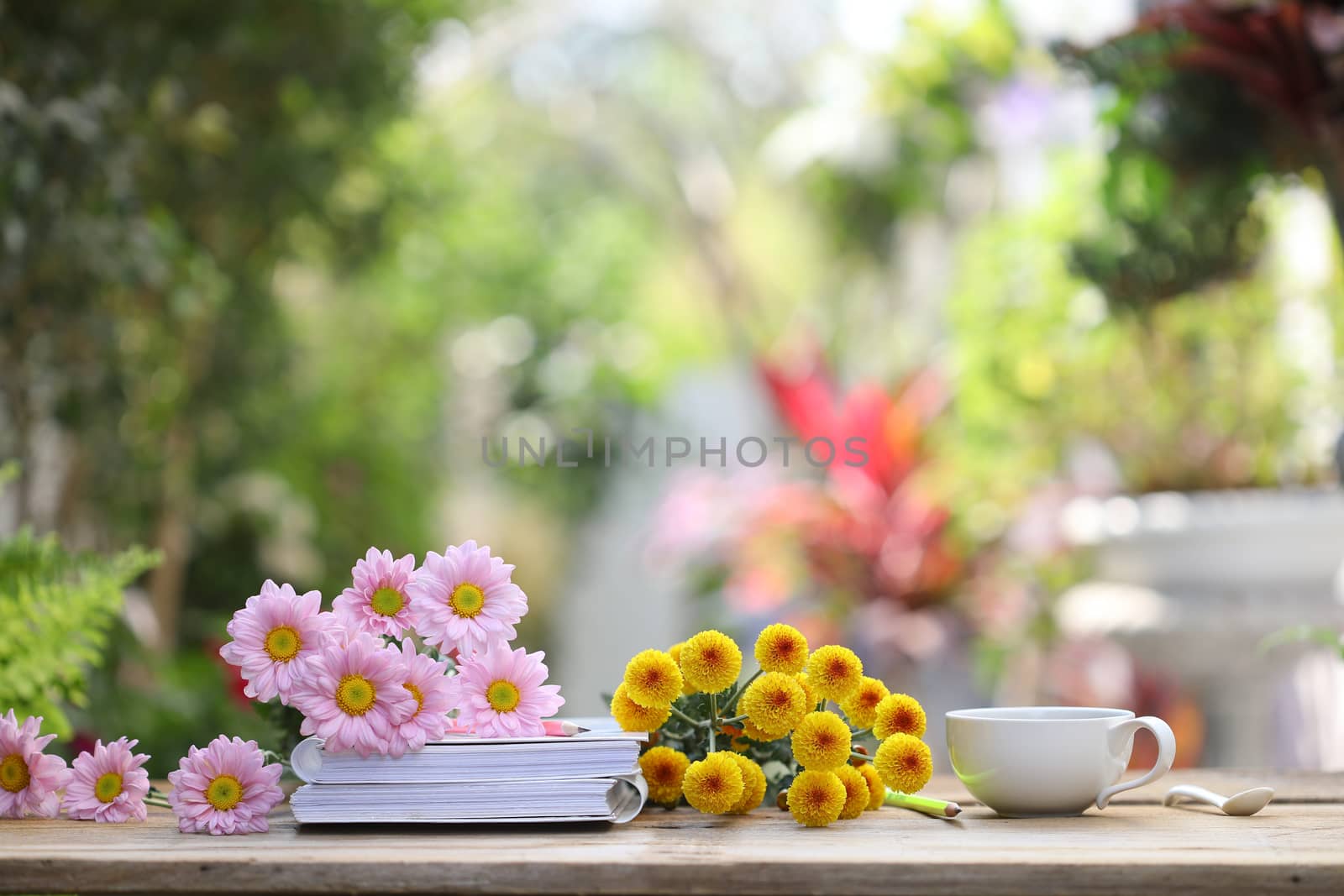 White coffee cup with white notebook and pink pencil with flowers on wooden table at outdoor