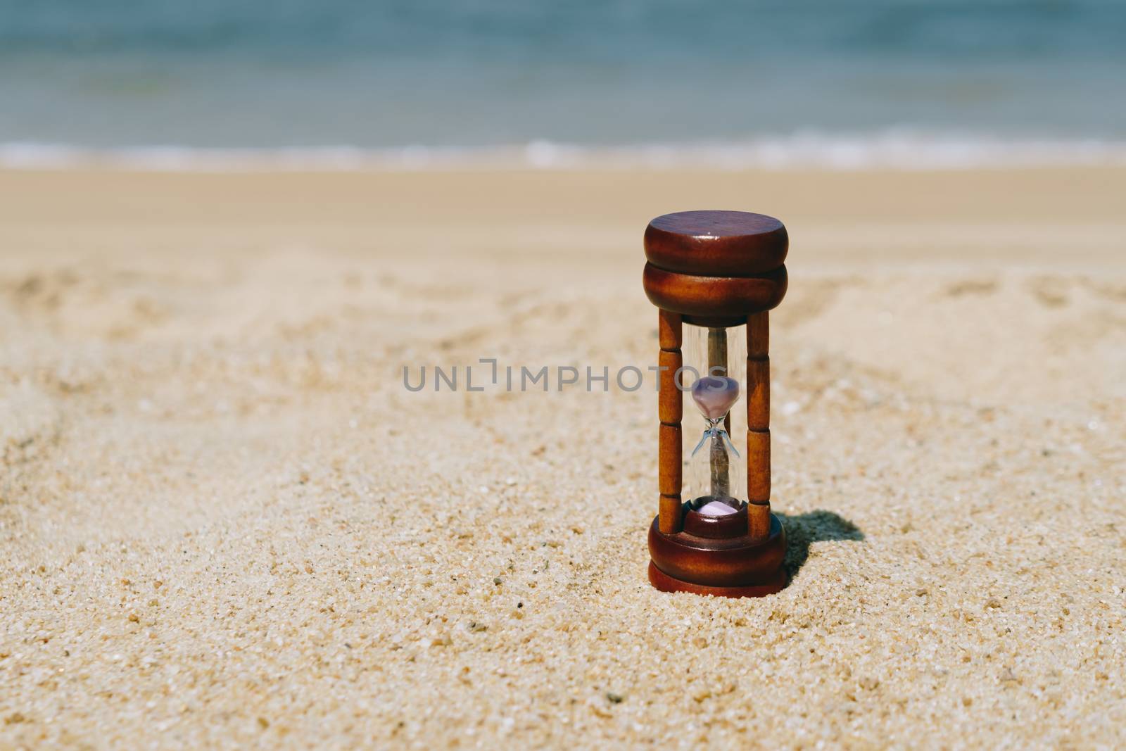 Small hourglass show time is flowing on sand beach texture background.