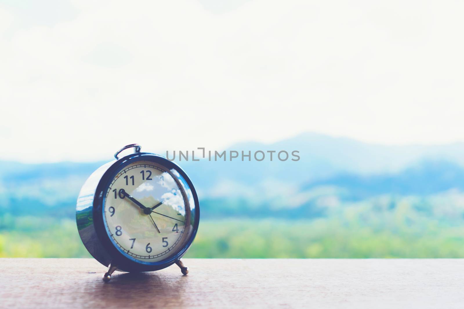 Selective focus of alarm clock on table with nature bokeh mountain background. Time in life concept