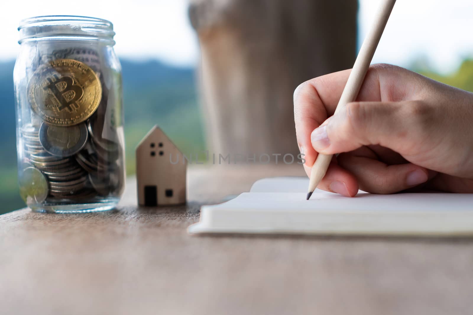 Woman hand writing down in small white memo notebook with jar full of money for plan wealth investing to do for future.