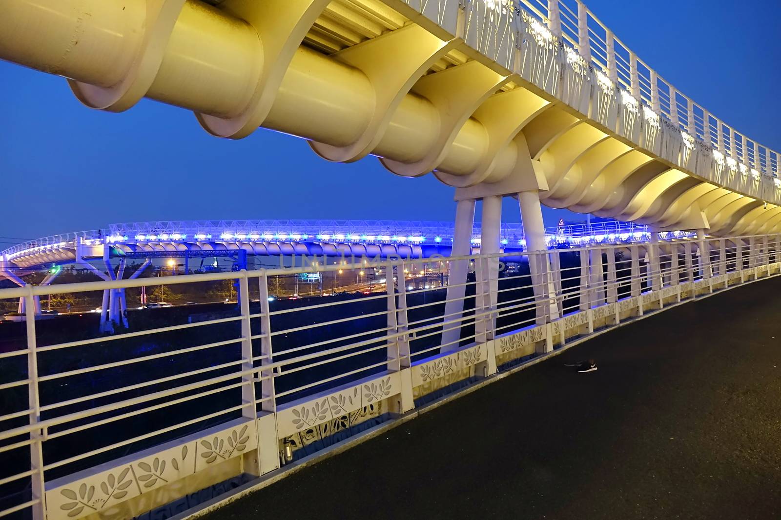A modern overpass for bikes and pedestrians lit up at evening time
