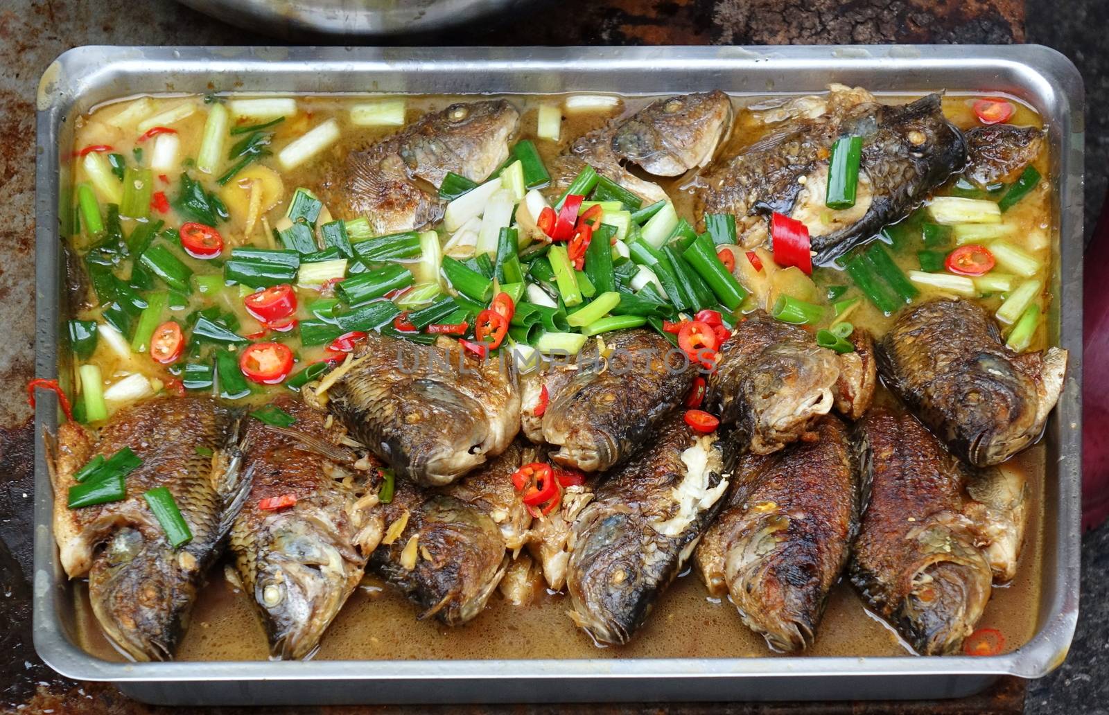 An outdoor food stall sells braised fish with chilies and scallion