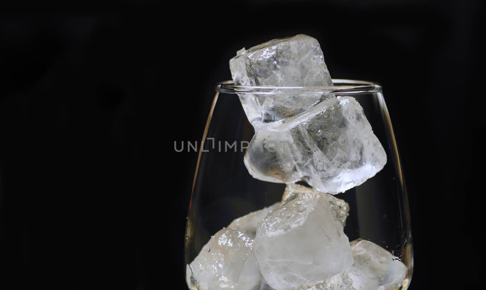 Making cocktail in a bar. Close up wine glass with ice cubes. Long cold drink.