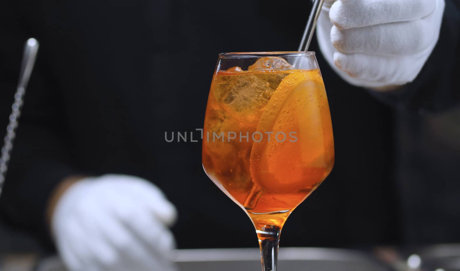 Close up ready-made Aperol Spritz Cocktail in wine glass. Hands of barman putting straw in the glass. Long fizzy drink.