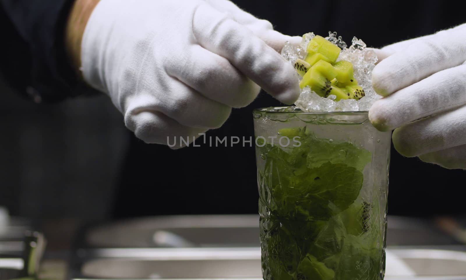 Classic Mojito Cocktail. Close up bartenders hand putting ice cup with kiwi on it. Long drink. Bar drinks series.