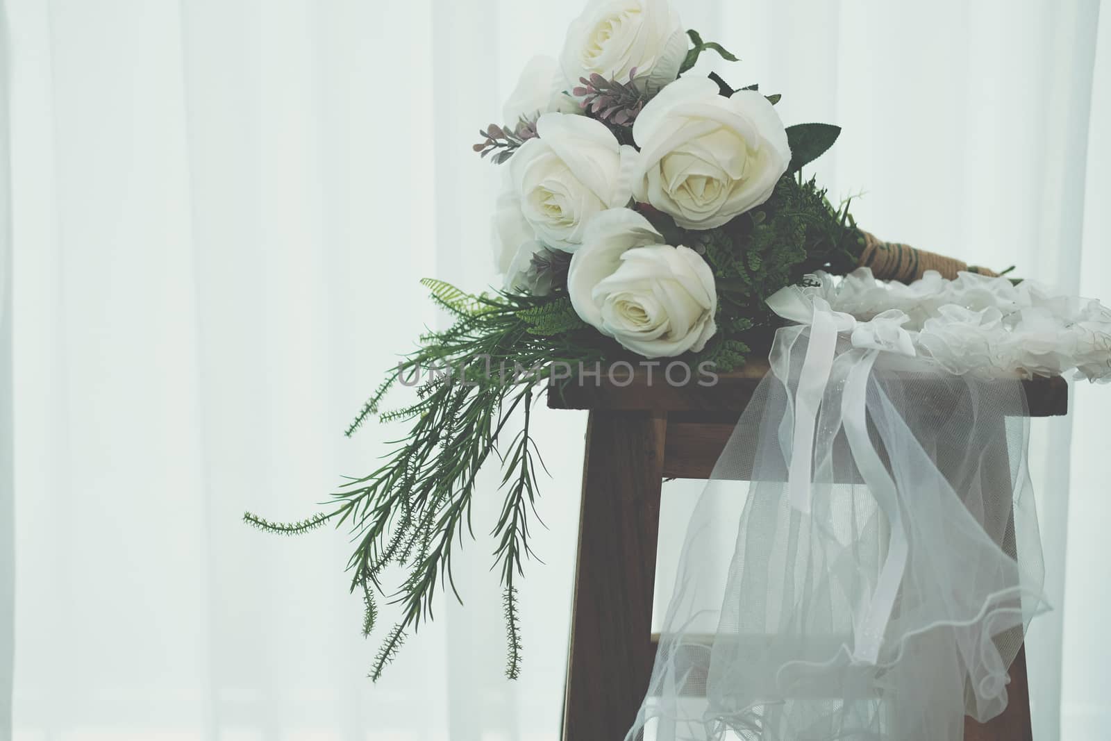 wedding white bridal veil & rose flower bouquet on wooden chair beside see through sheer window curtain