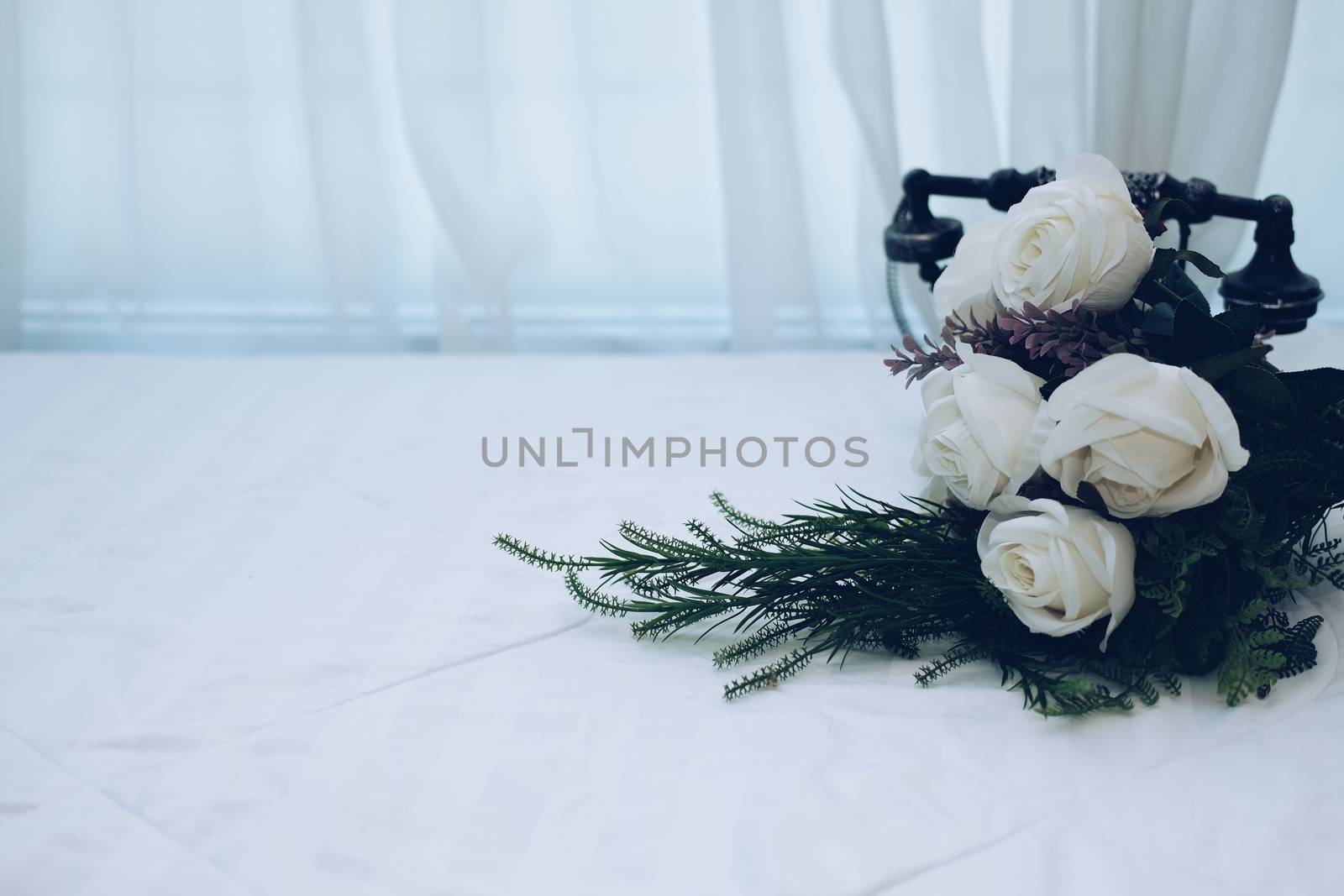white bridal wedding rose flower bouquet on bed beside see through sheer window curtain
