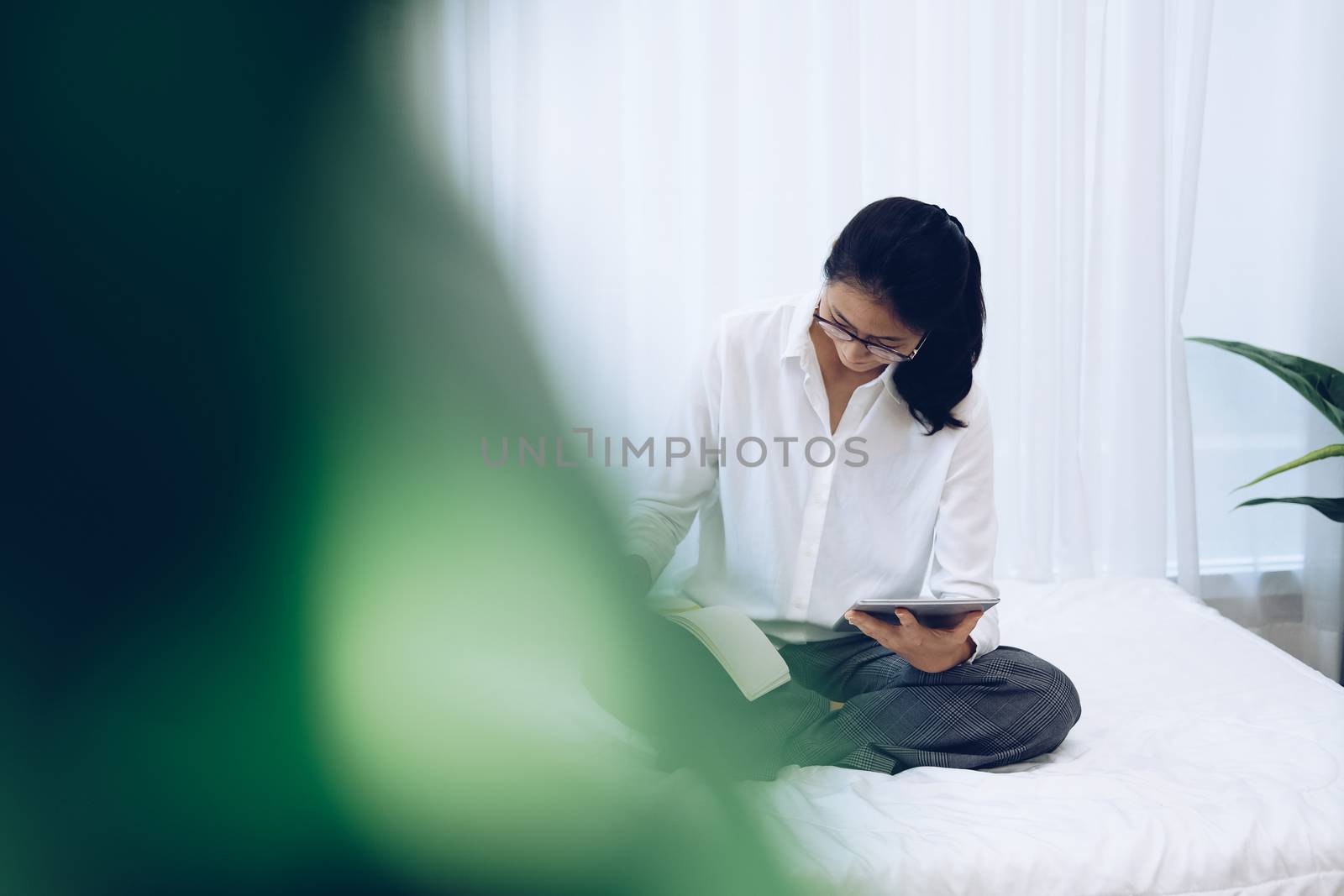 asian woman writing note watching video on tablet. student listen lecture study online course on bed in bedroom at home