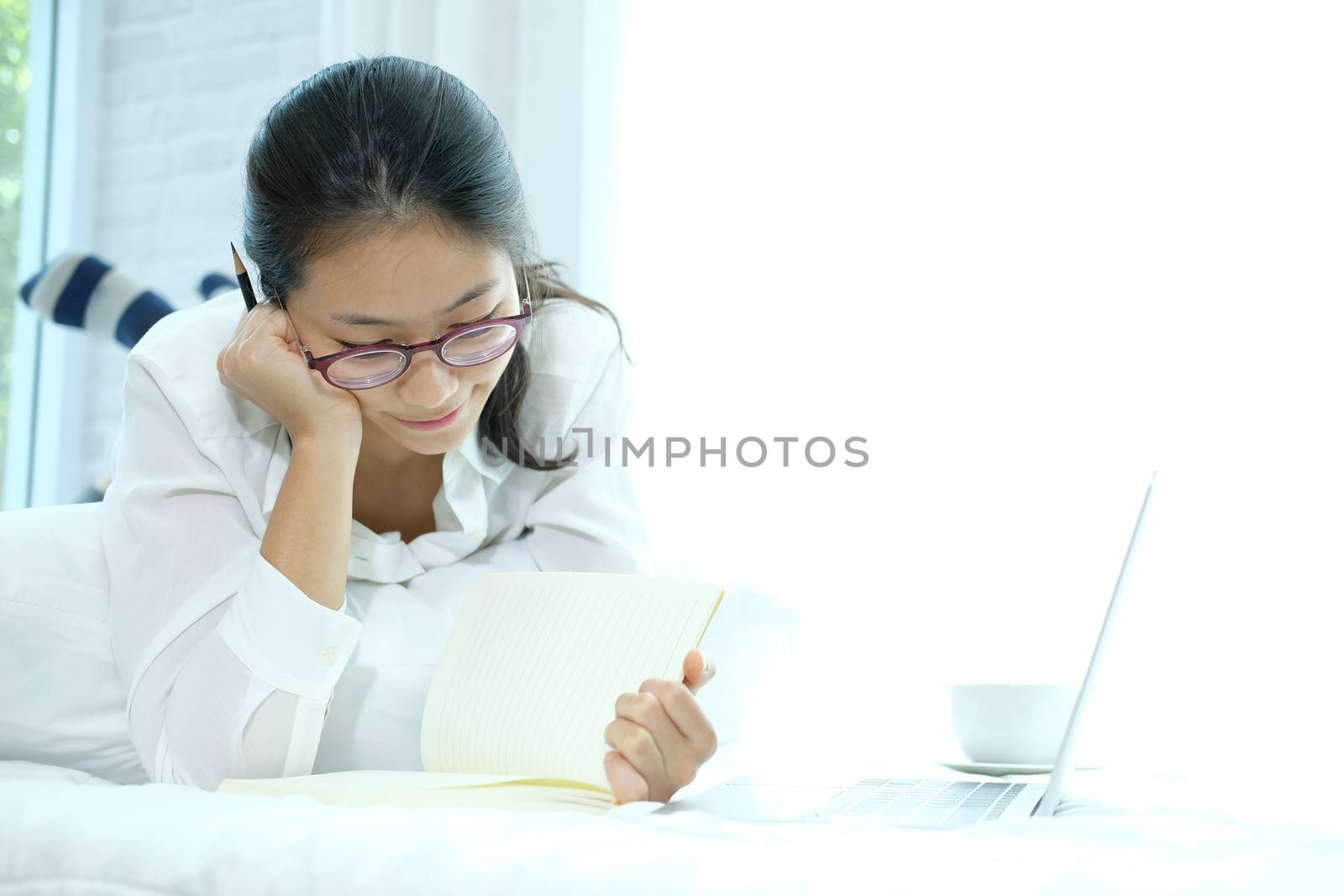 asian woman writing note working with computer laptop on bed. student listen lecture learning studying online in bedroom.