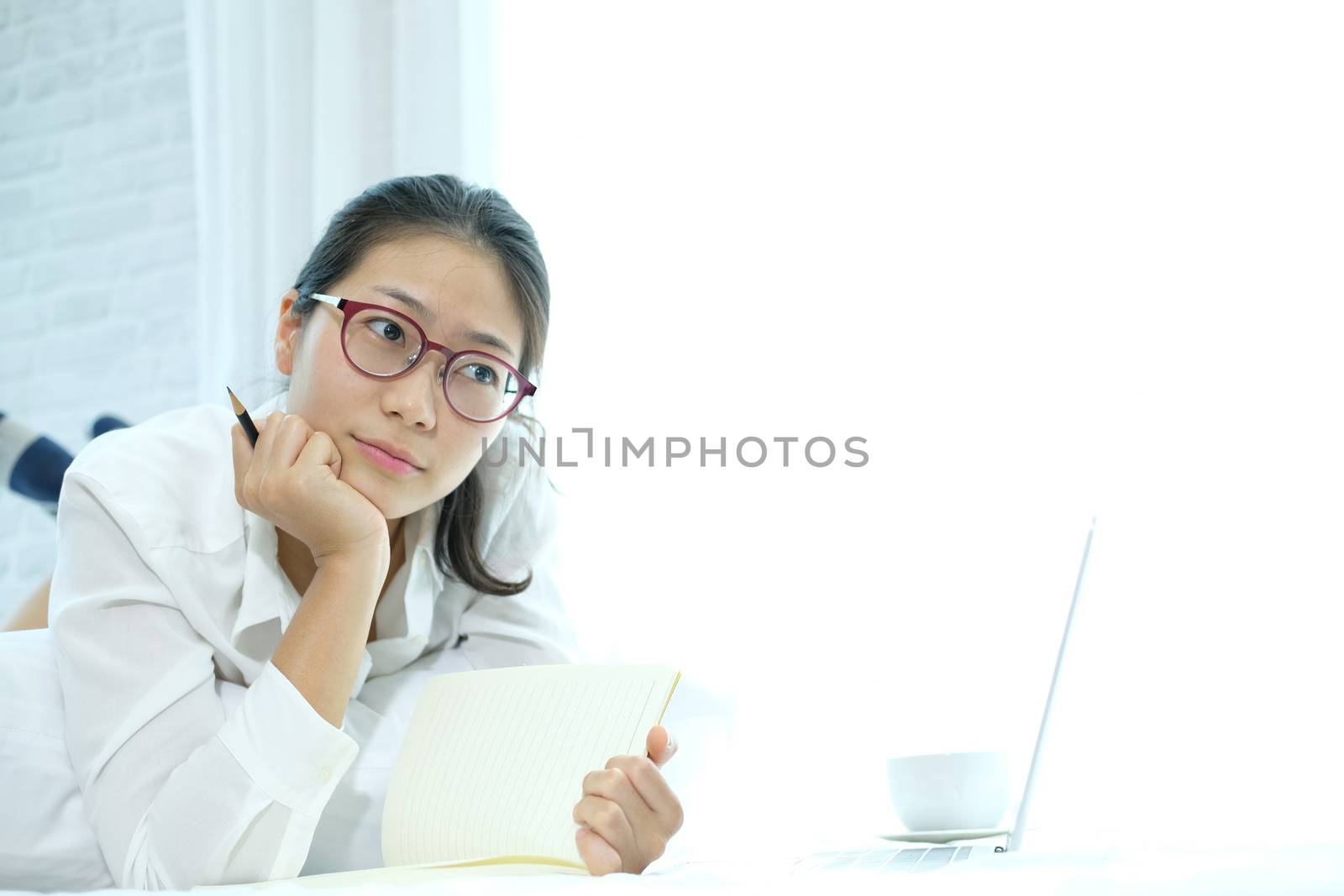 asian woman writing note working with computer laptop on bed. student listen lecture learning studying online in bedroom.