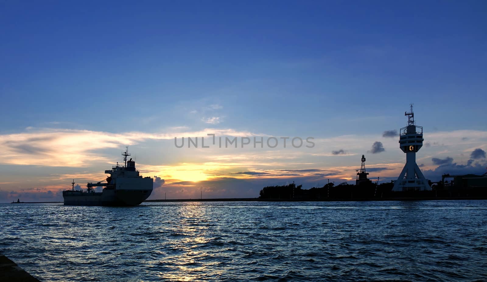 A large cargo ship leaves Kaohsiung Port at sunset
