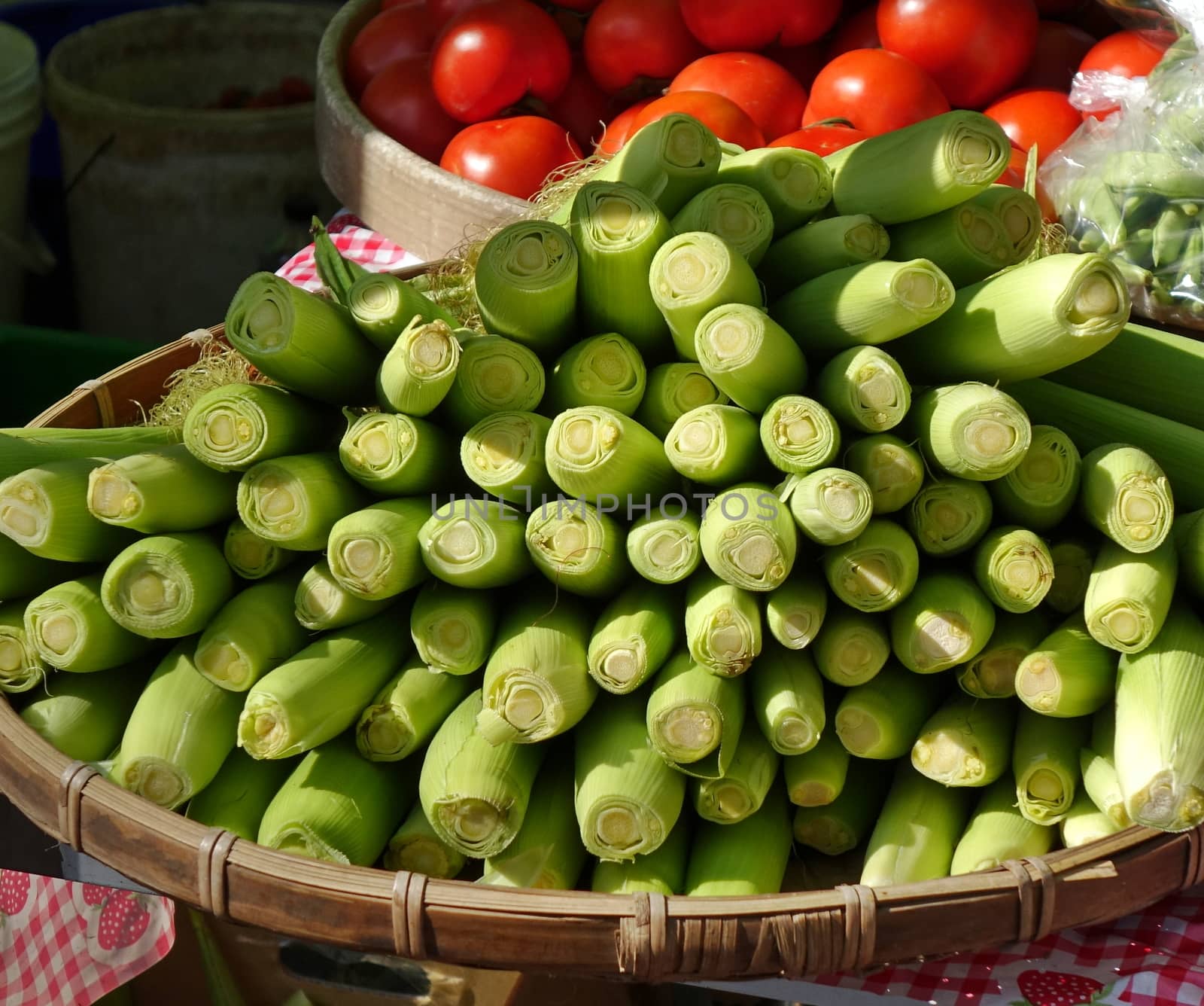 A market stall sells fresh baby corn and ripe red tomatoes
