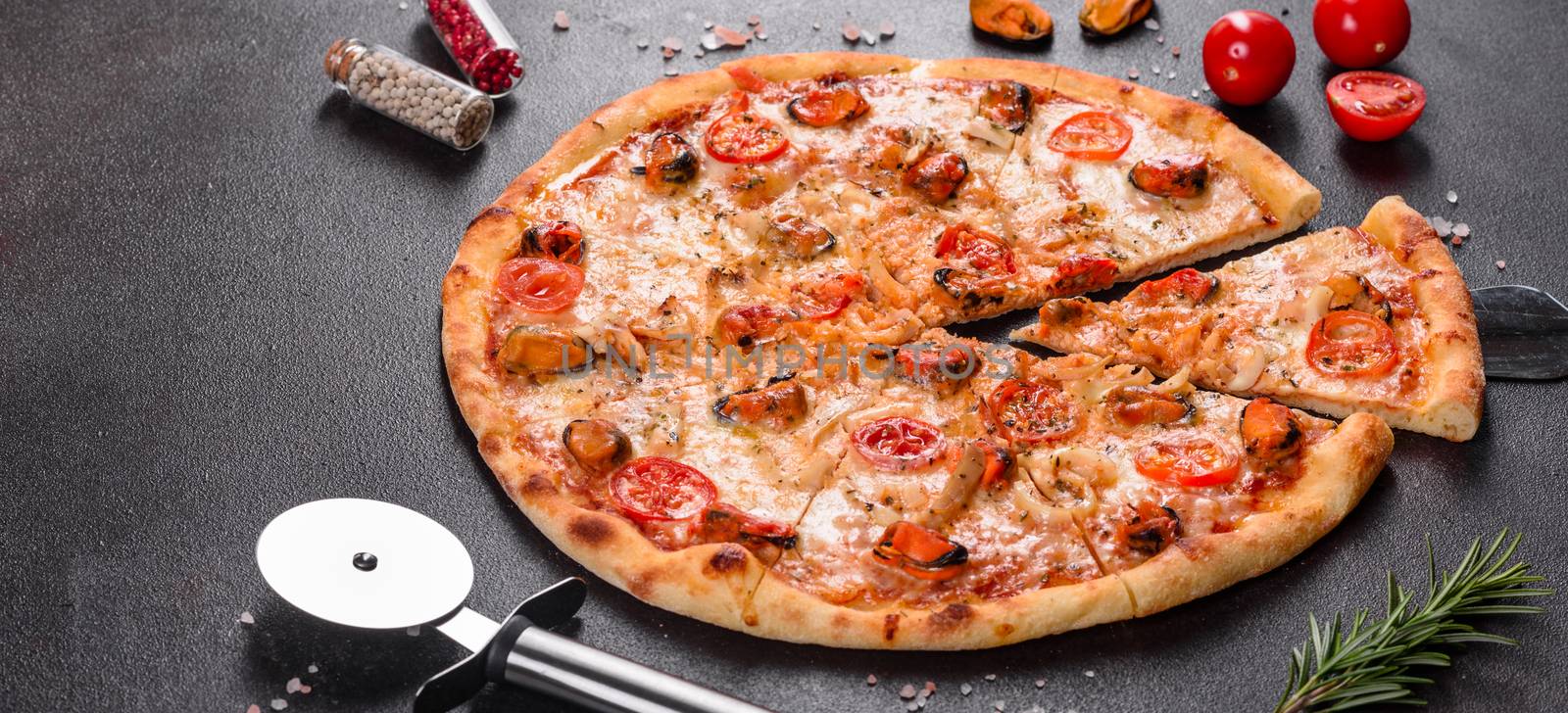 Seafood Italian pizza with shrimp, squid, mussels, fresh herbs and mozzarella on a
dark background. Tasty sliced pizza with seafood and tomato on a concrete background