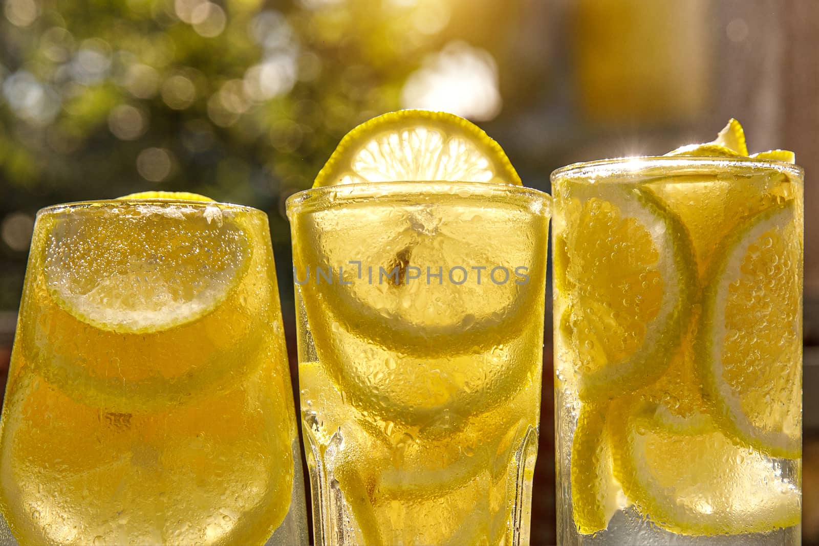Three glasses of lemon water on the sunny garden background. Close-up view