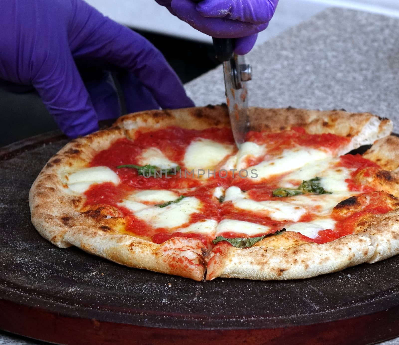 Pizza margherita with tomatoes, cheese and fresh basil is being cut before serving