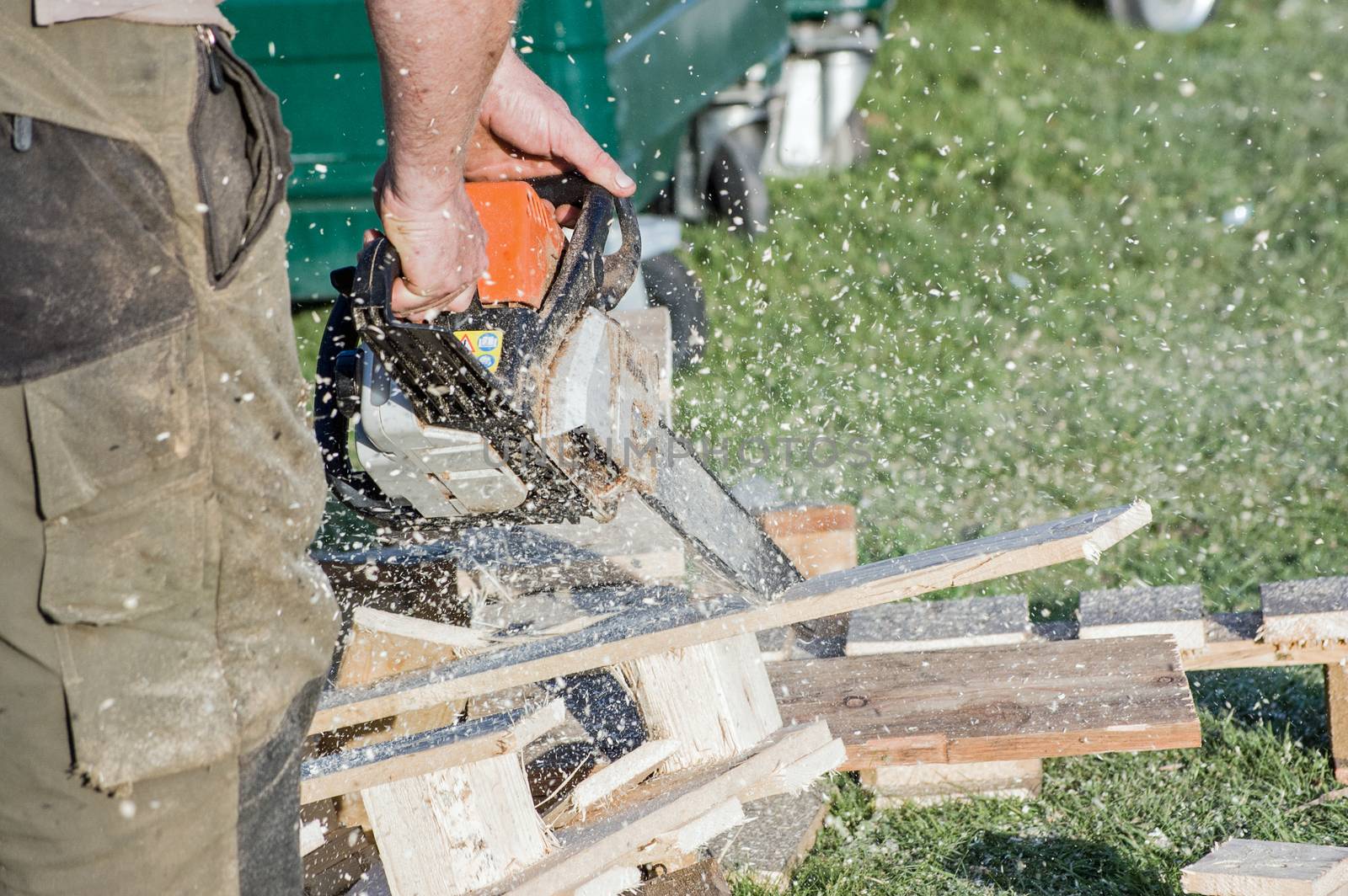 A man using a chainsaw to cut through wooden pallets with sawdust spraying .