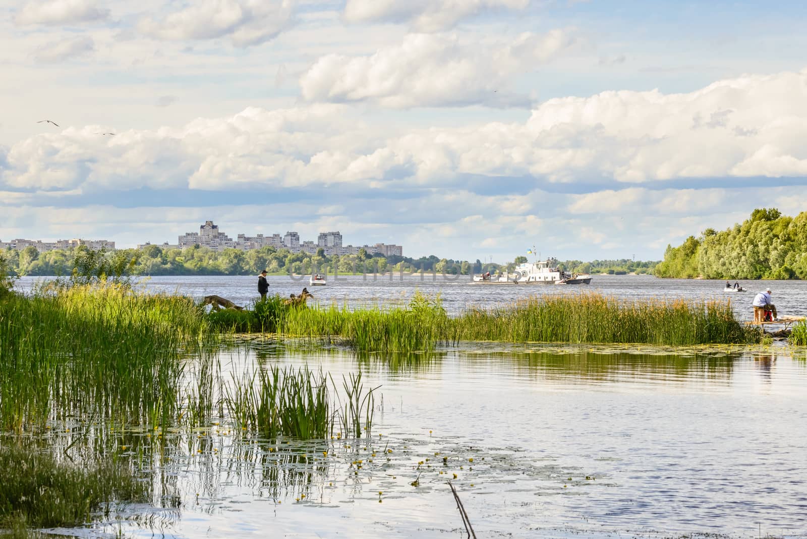 KIEV/UKRAINE - JUNE 18, 2014 - Fishers and a white boat on the Dnieper River in Kiev, Ukraine. A view of the city in the distance, under a spring cloudy sky.