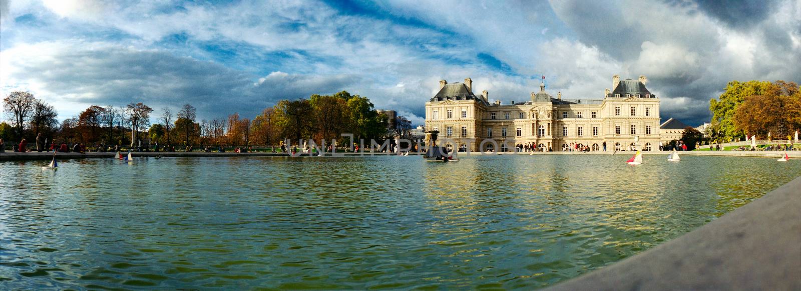 panoramic view of the fountain of jardin de Luxembourg in warm autumnal light and a blue sky with some wooden little boats on it