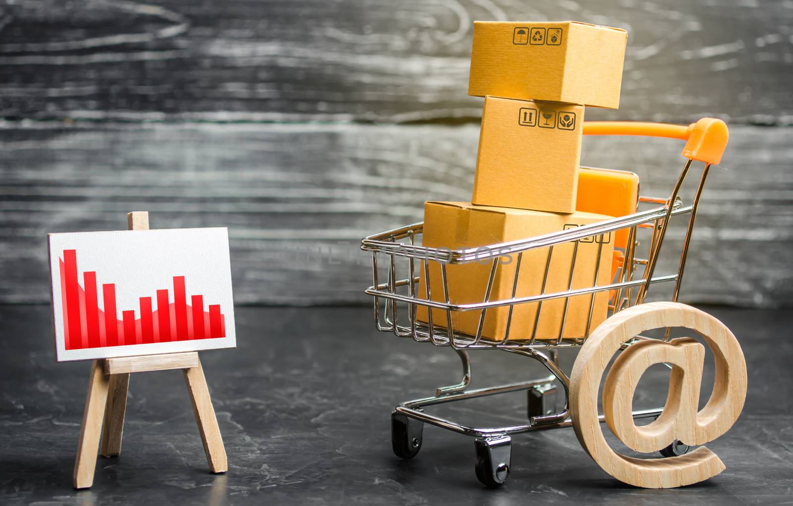 Shopping cart loaded with boxes, email symbol and red negative trend chart. Reduced online sales over the Internet. Fall in purchasing power. Price reduction. Decline in sales and business activity by iLixe48