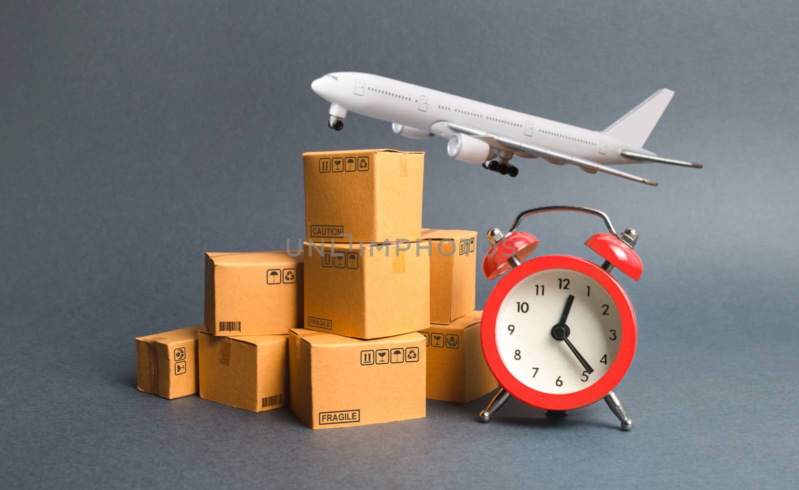 Cargo plane, stack of cardboard boxes and a red alarm clock. Express air delivery concept. Temporary storage, limited offer and discount. Optimization of logistics, improving efficiency