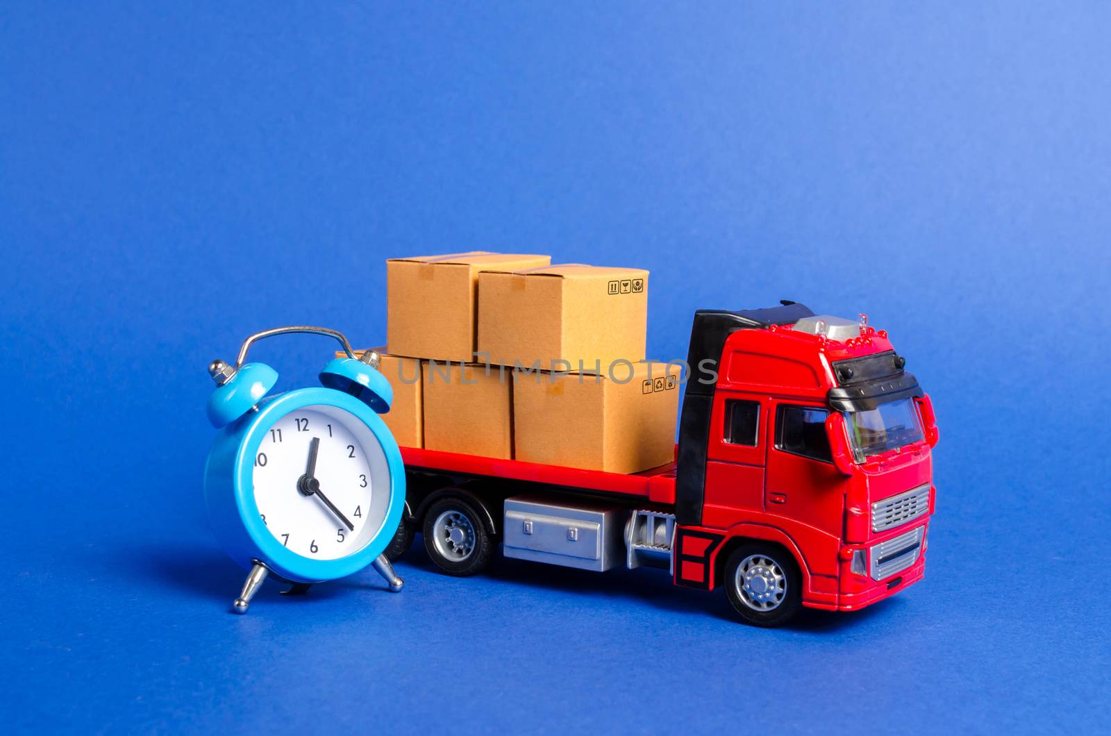 A red truck with cardboard boxes and a blue alarm clock. Express delivery in short time concept. Temporary storage, limited offer and discount. Optimization of delivery logistics. Transport company by iLixe48