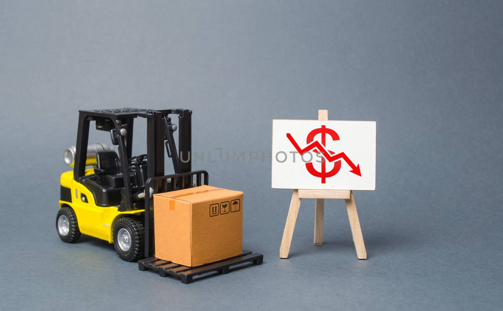 Forklift truck carries a cardboard box near a stand with a red dollar arrow down. decline in the production of goods and products, economic downturn and recession. Falling consumer demand.