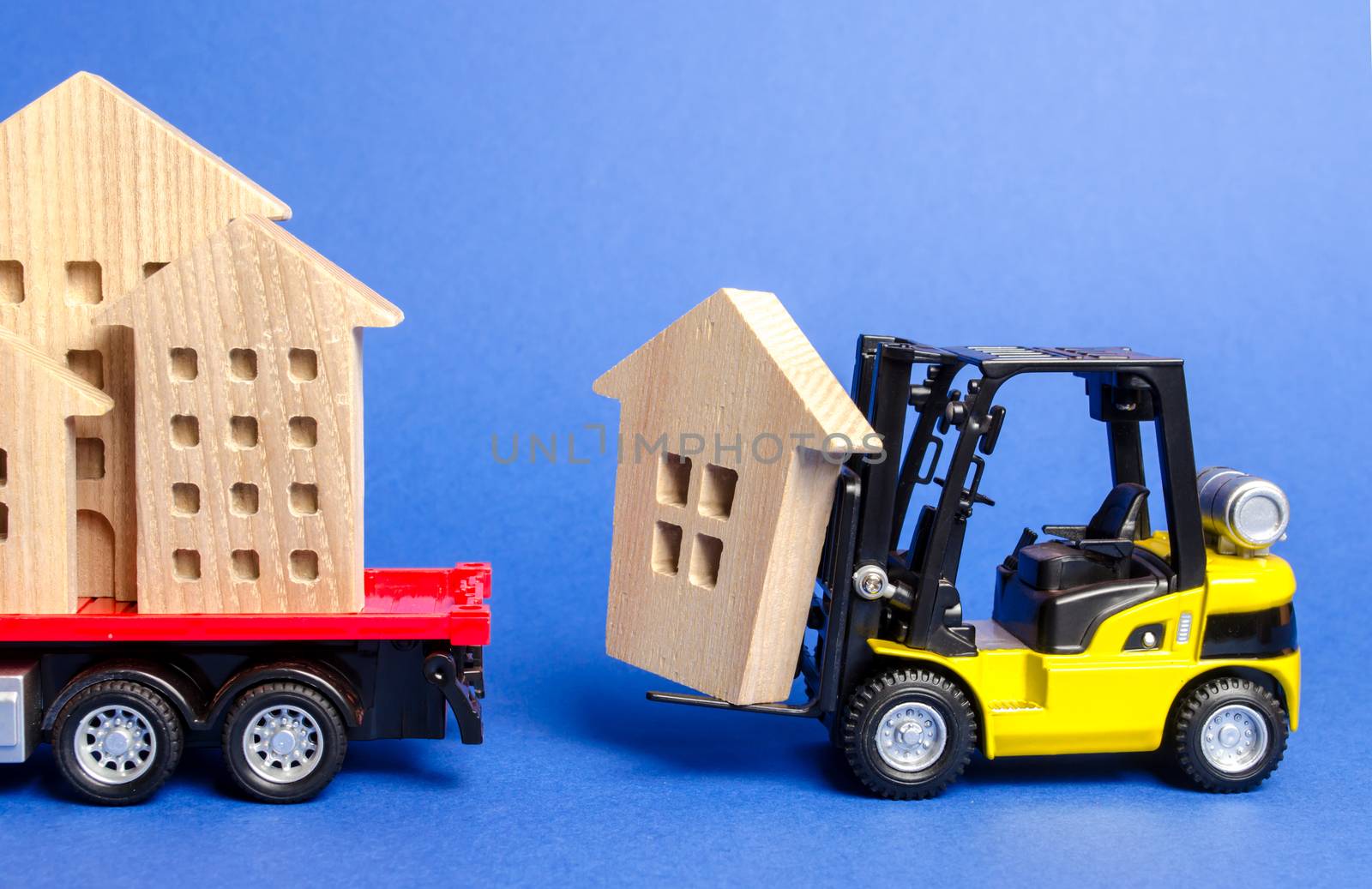 A yellow forklift loads a wooden figure of a house into a truck. Concept of transportation and cargo shipping, moving company. Construction of new houses and objects. Industry. Move entire buildings. by iLixe48