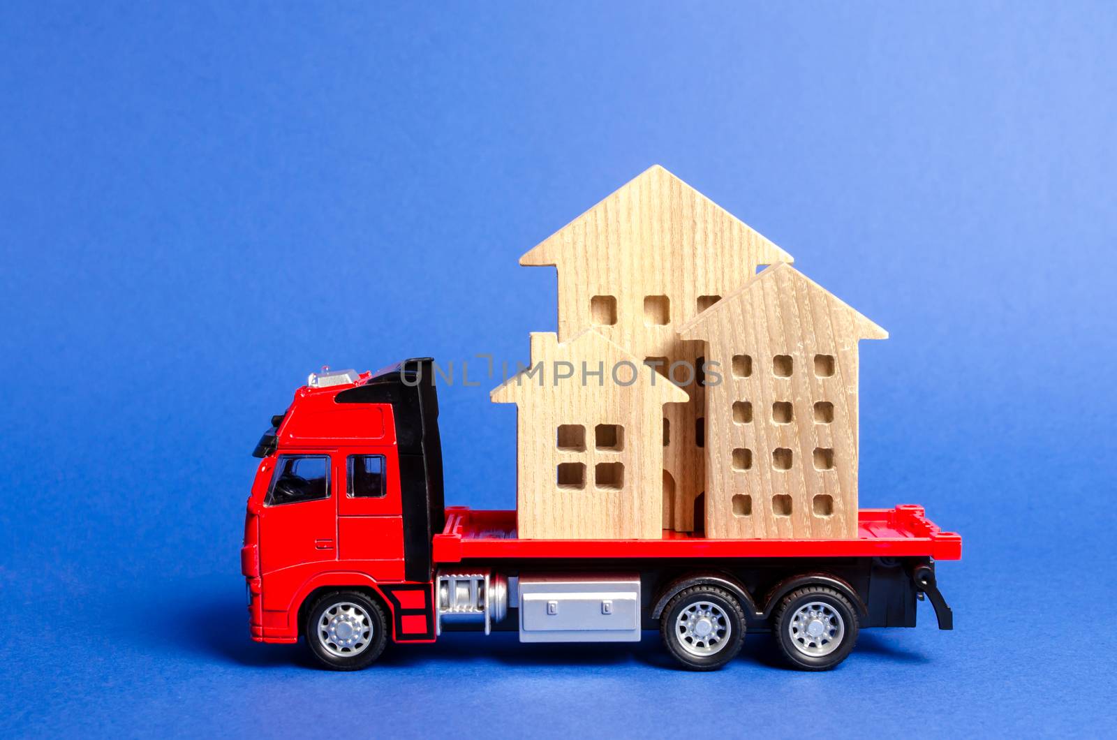 Red truck transports wooden houses. Concept of transportation and cargo shipping, moving company. Construction of new houses and objects. Industry. Logistics and supply. Move entire buildings.