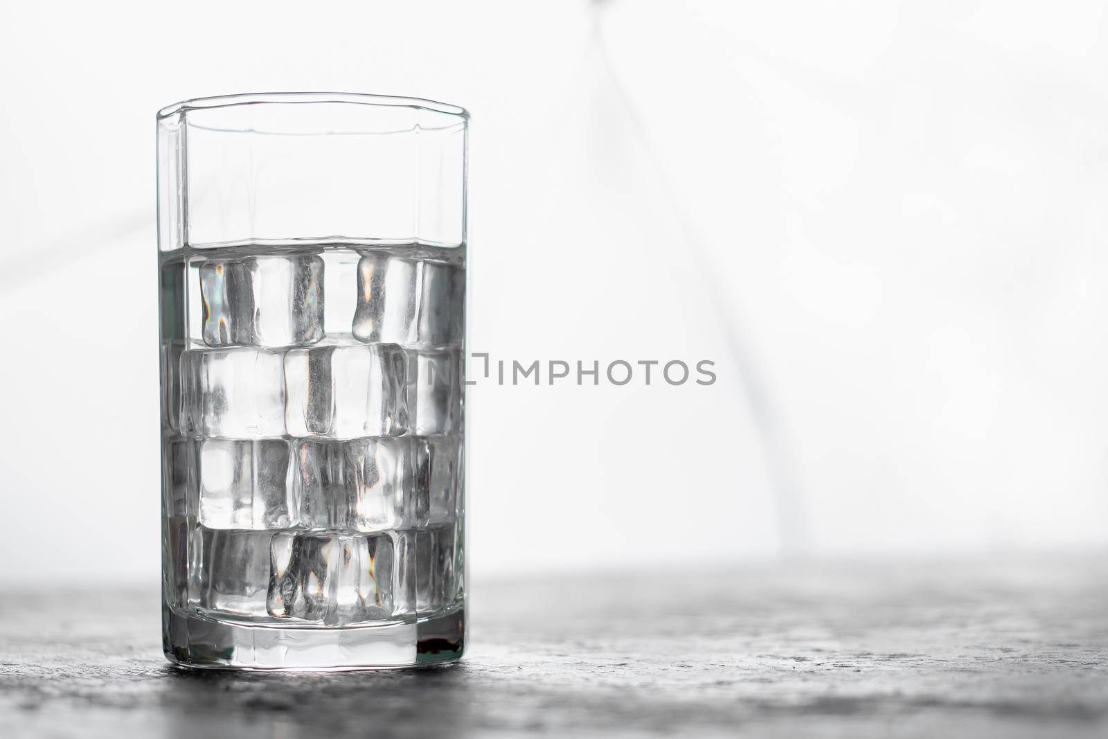 Glass of water with ice and light blurred background.