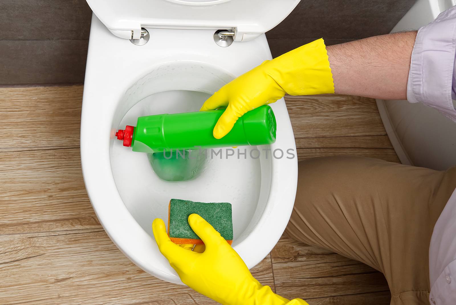 Man disinfecting the toilet seat by spraying a green sanitizer from a bottle. A man disinfects a toilet at home. by PhotoTime