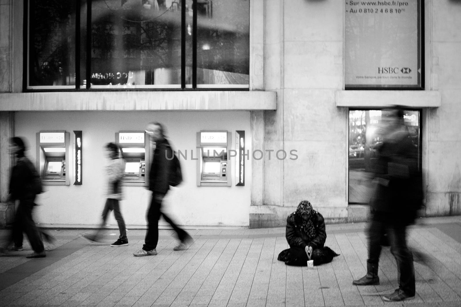 A homeless person begging on the street while people walk by