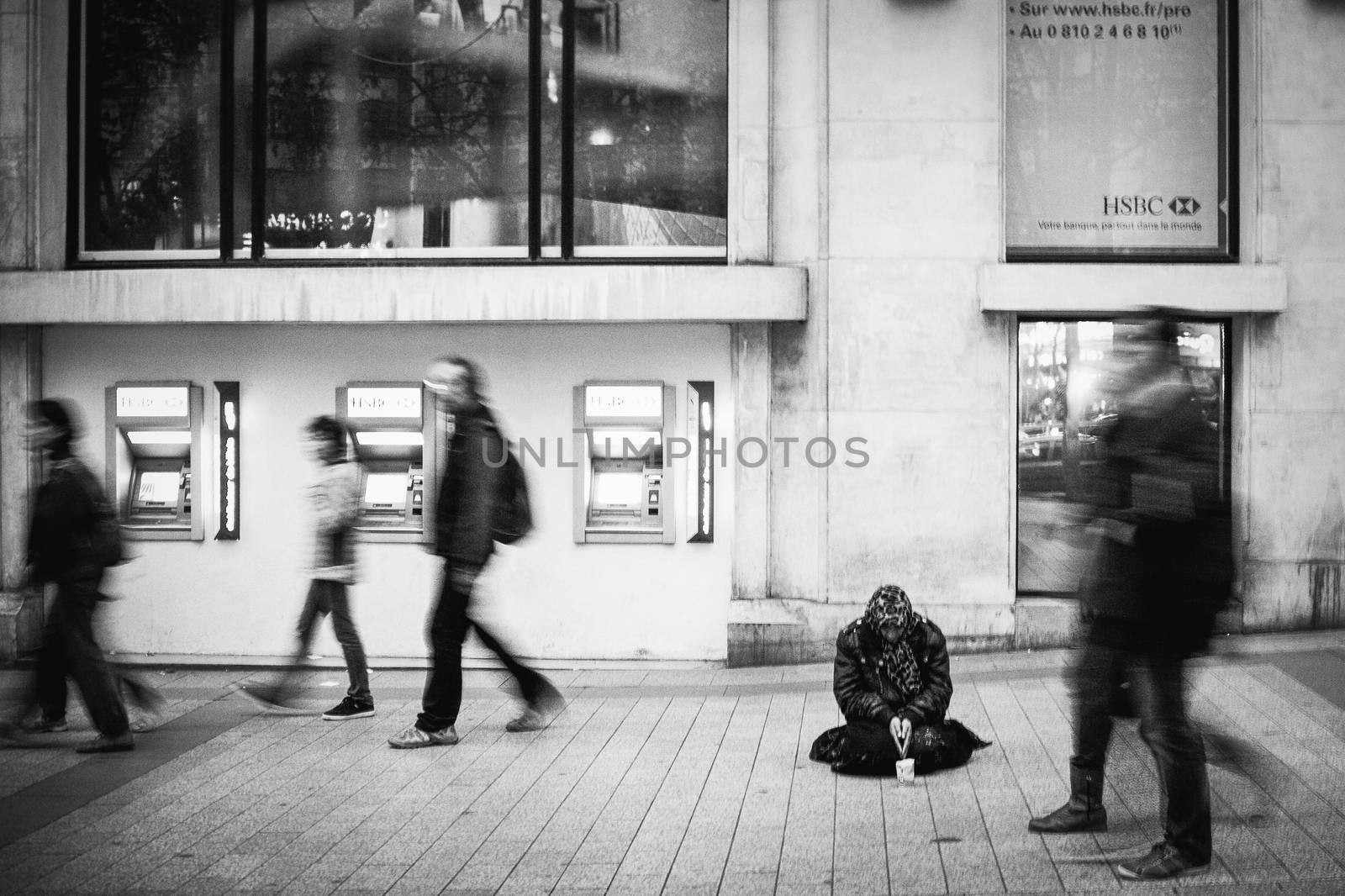 A homeless person begging on the street while people walk by