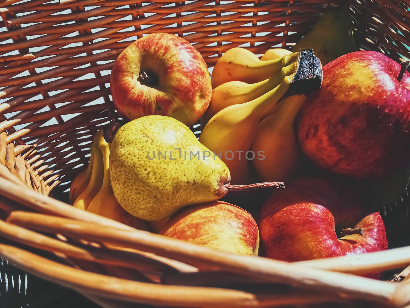 Organic apples, pears and bananas on rustic in a wicker basket by Anneleven