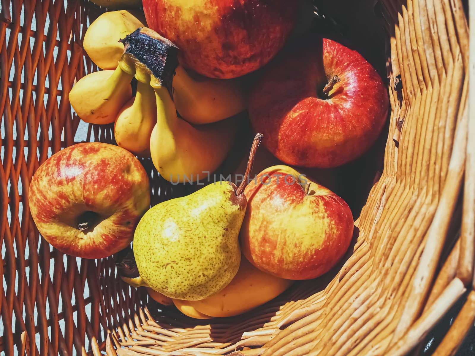 Organic apples, pears and bananas on rustic in a wicker basket by Anneleven