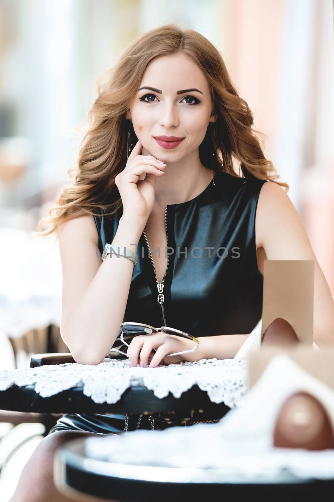 Attractive young caucasian woman sitting in street cafe, waiting for someone, having coffee, having great time. She wearing black stylish dress,