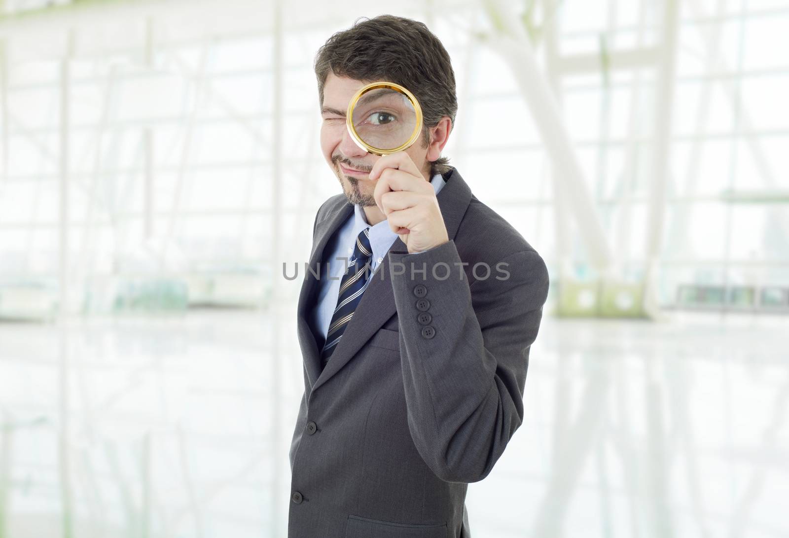 Isolated young business man with magnifying glass, at the office