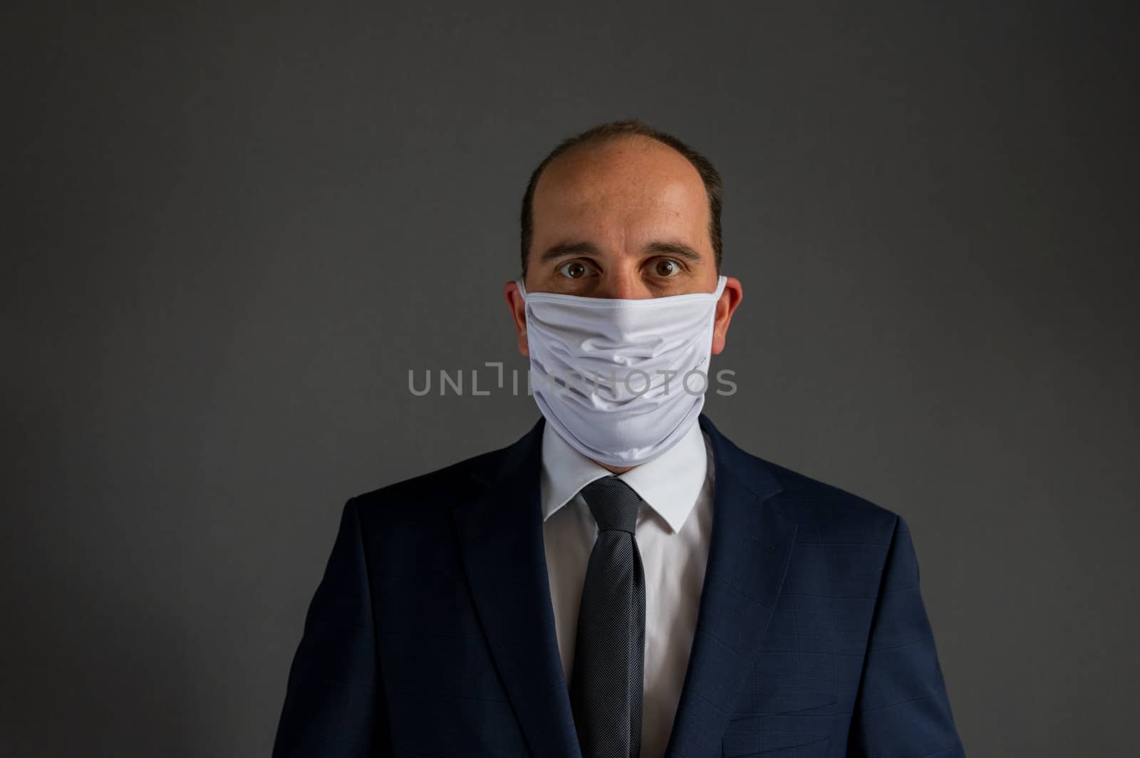 portrait of a smart dressed business man with suit and tie wearing a protective face mask looks into the camera. Gray Background with lots of copy space