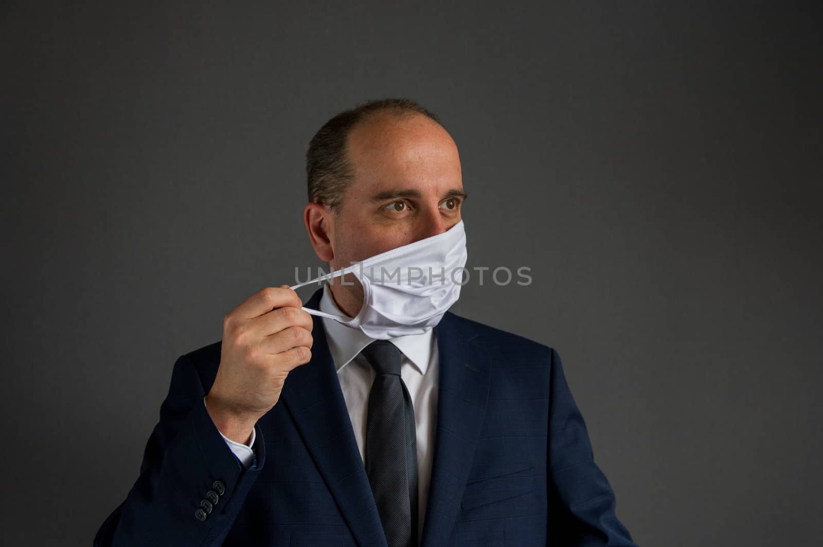 portrait of a smart dressed business man with suit and tie taking off his protective face mask looks into the distance off camera. Concept of hope for businesses and enterprises after corona epidemic