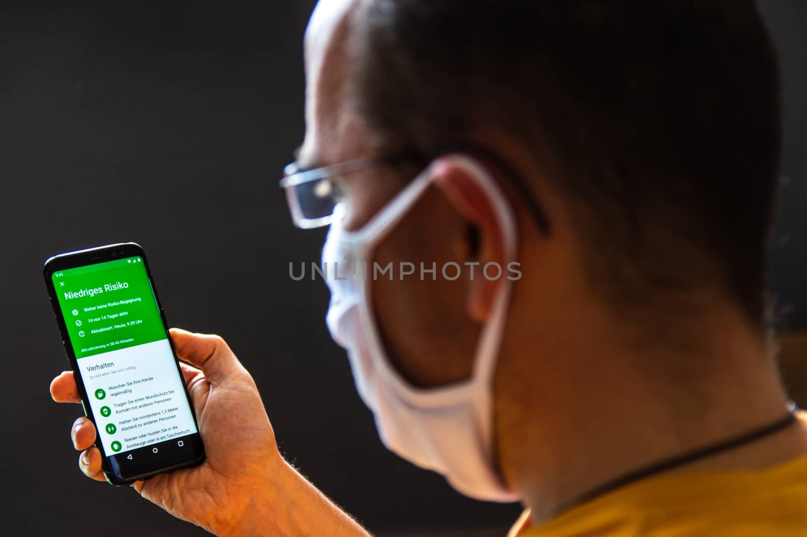 Zittau, Saxony / Germany, June 5th 2020: Young man wearing a protective face mask checks the German corona warn app for his infection risk analysis. Niedriges Risiko = German for Low Risk, Shallow DOF