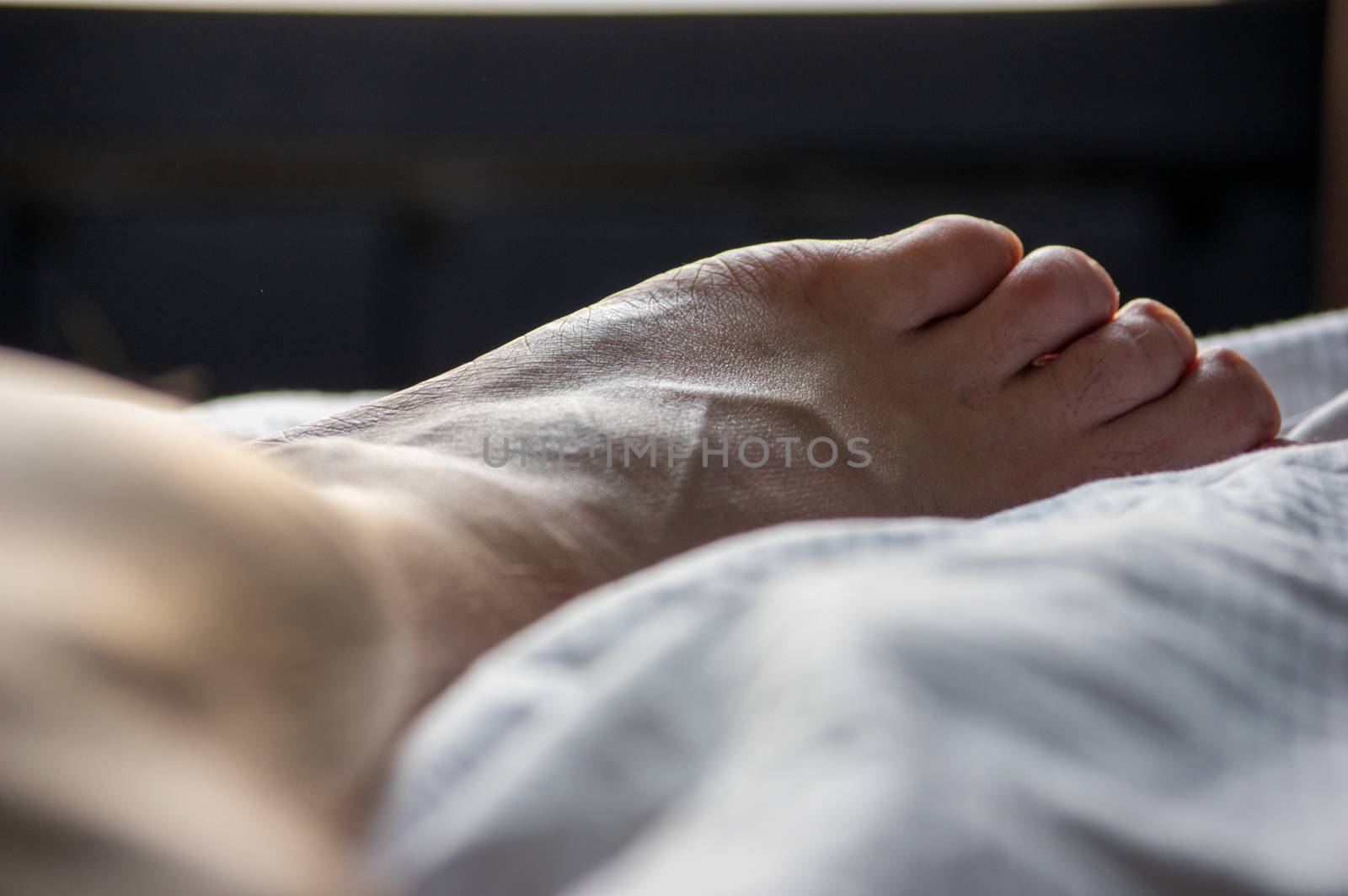 Close-up of male leg and foot lying on a bed in a hotel room looking out of a window