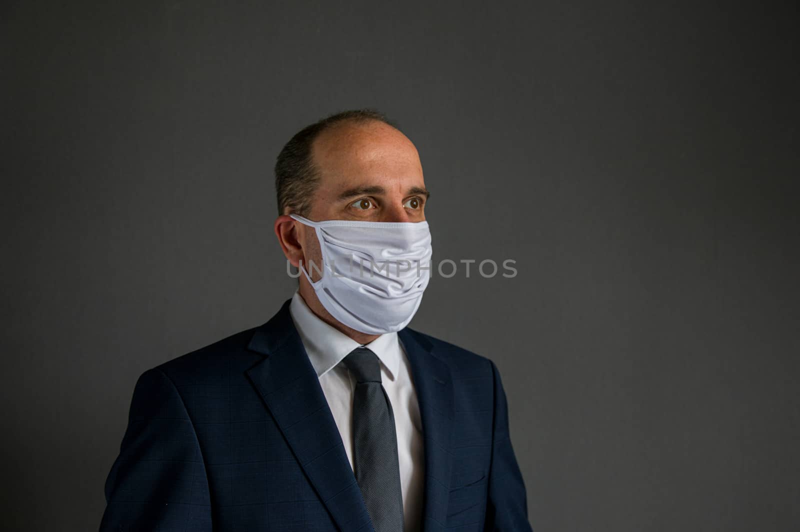 portrait of a smart dressed business man with suit and tie and protective face mask looks into the distance off camera. Concept of hope for businesses and enterprises after corona epidemic