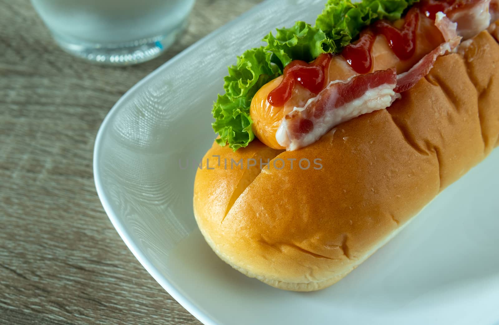 Ham sausage sandwich topped with ketchup on a white plate on the table, simple food. Top view