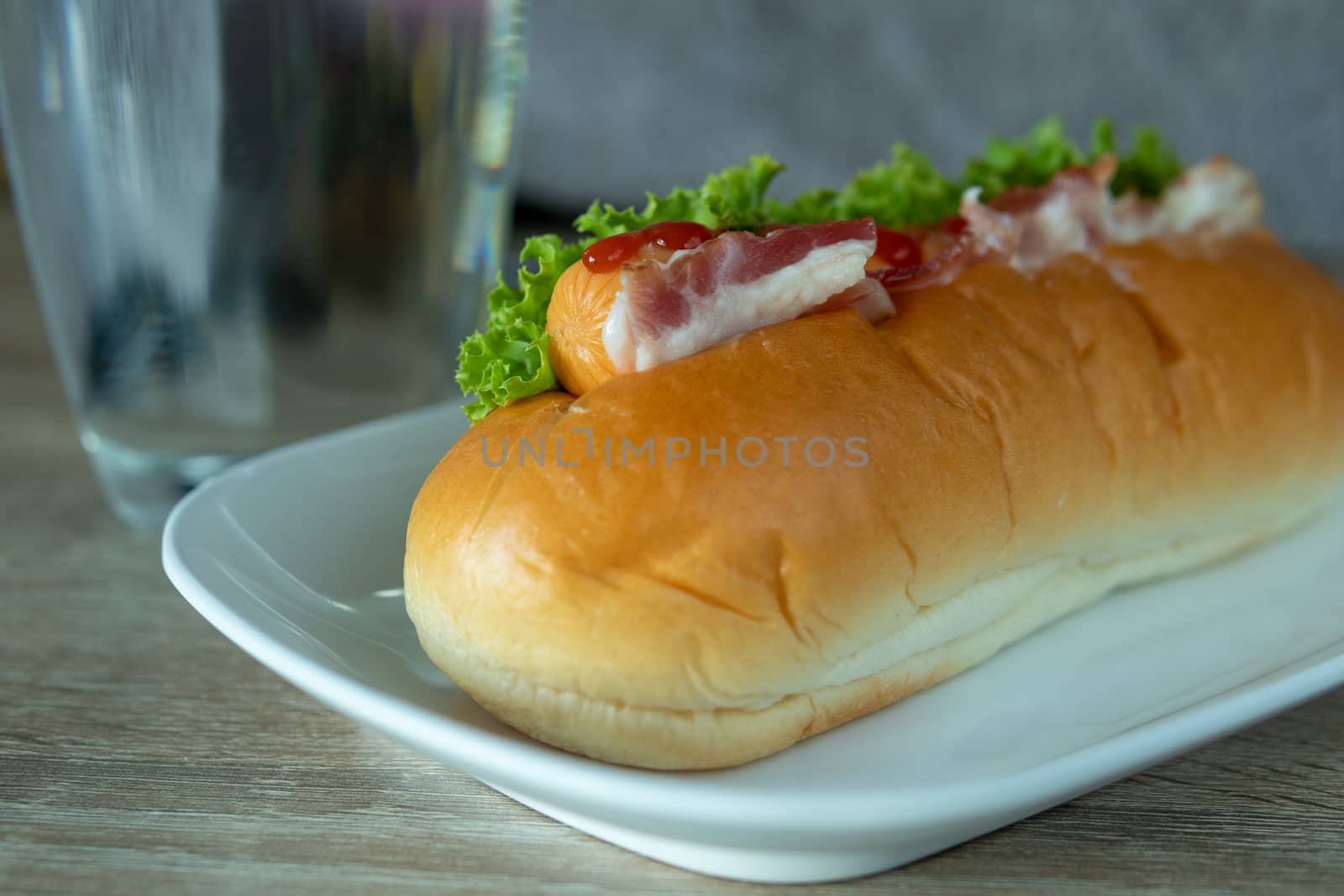 Ham sausage sandwich topped with ketchup on a white plate on the table, simple food