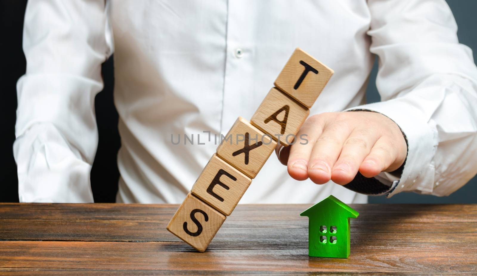 A man protects his hand with a figurine of a house from a falling tower of cubes with the word taxes. Heavy tax burden, protecting the interests of small and medium-sized businesses, competitiveness.
