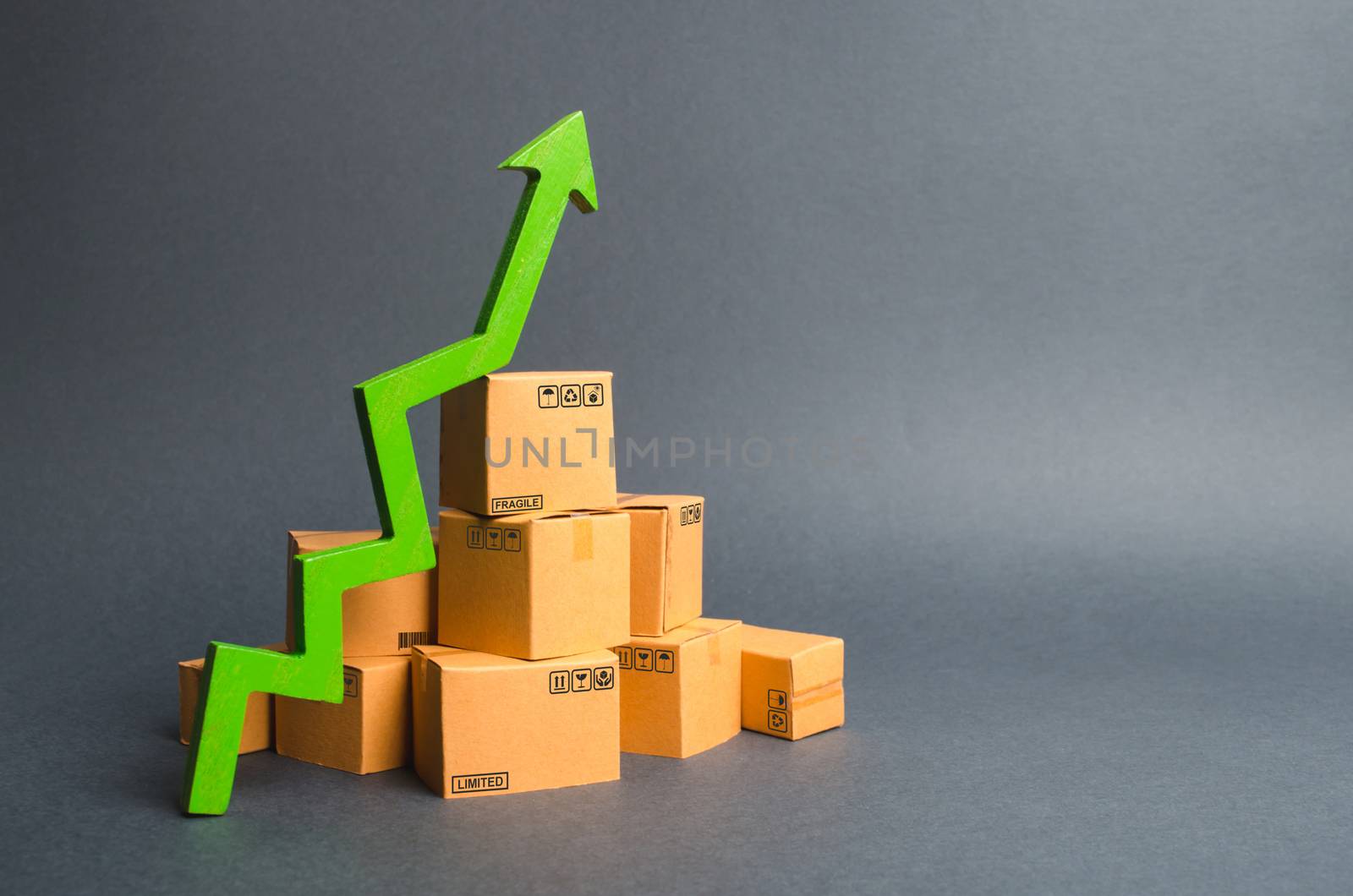 A pile of cardboard boxes and a green up arrow. The growth rate of production of goods and products, increasing economic indicators. Increasing consumer demand, increasing exports or imports.