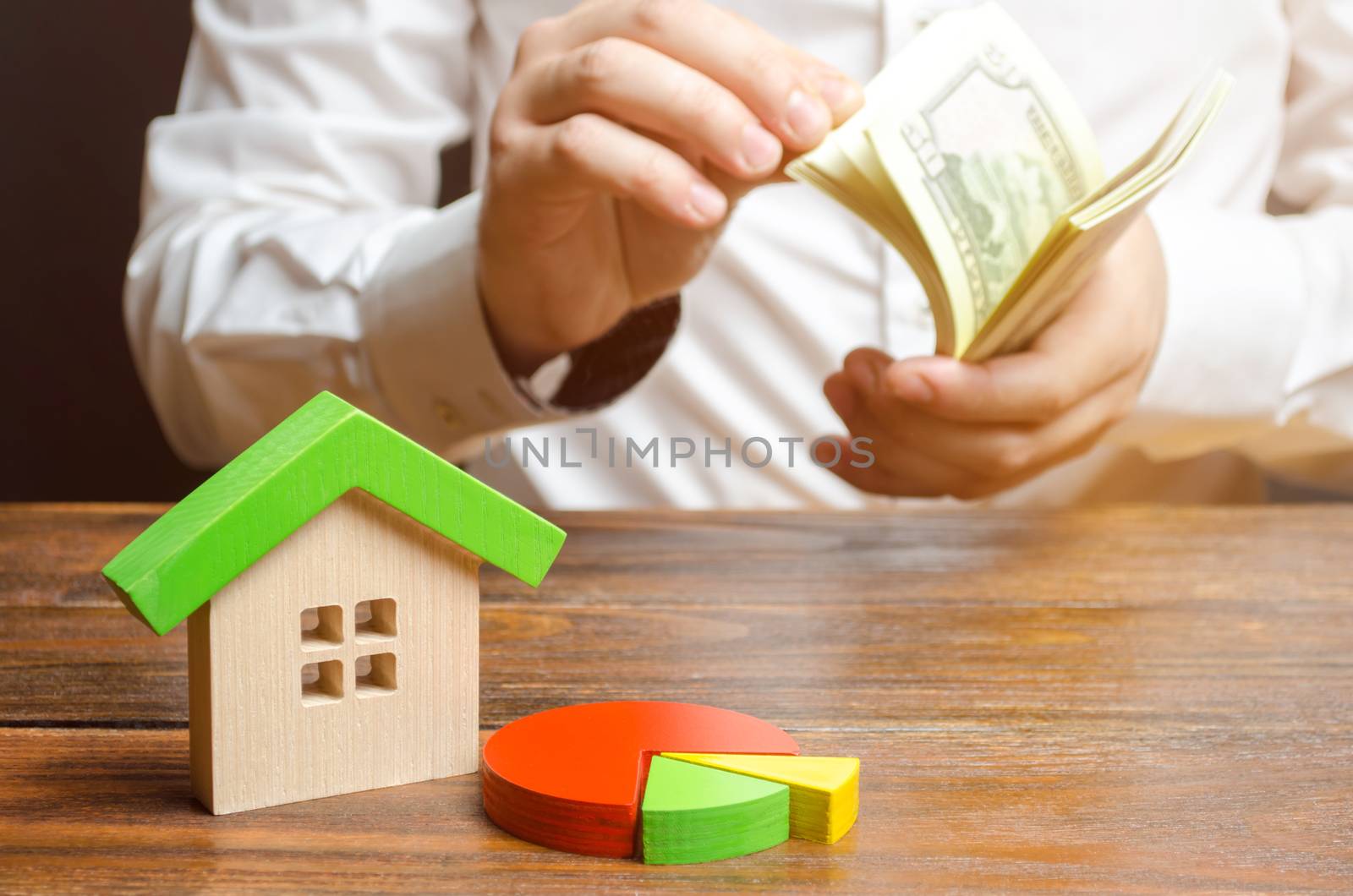 House figurine and pie chart on the background of a man counting money. Micromanagement and cost structure for maintaining a home and paying bills. Buying a house in installments, credit. by iLixe48