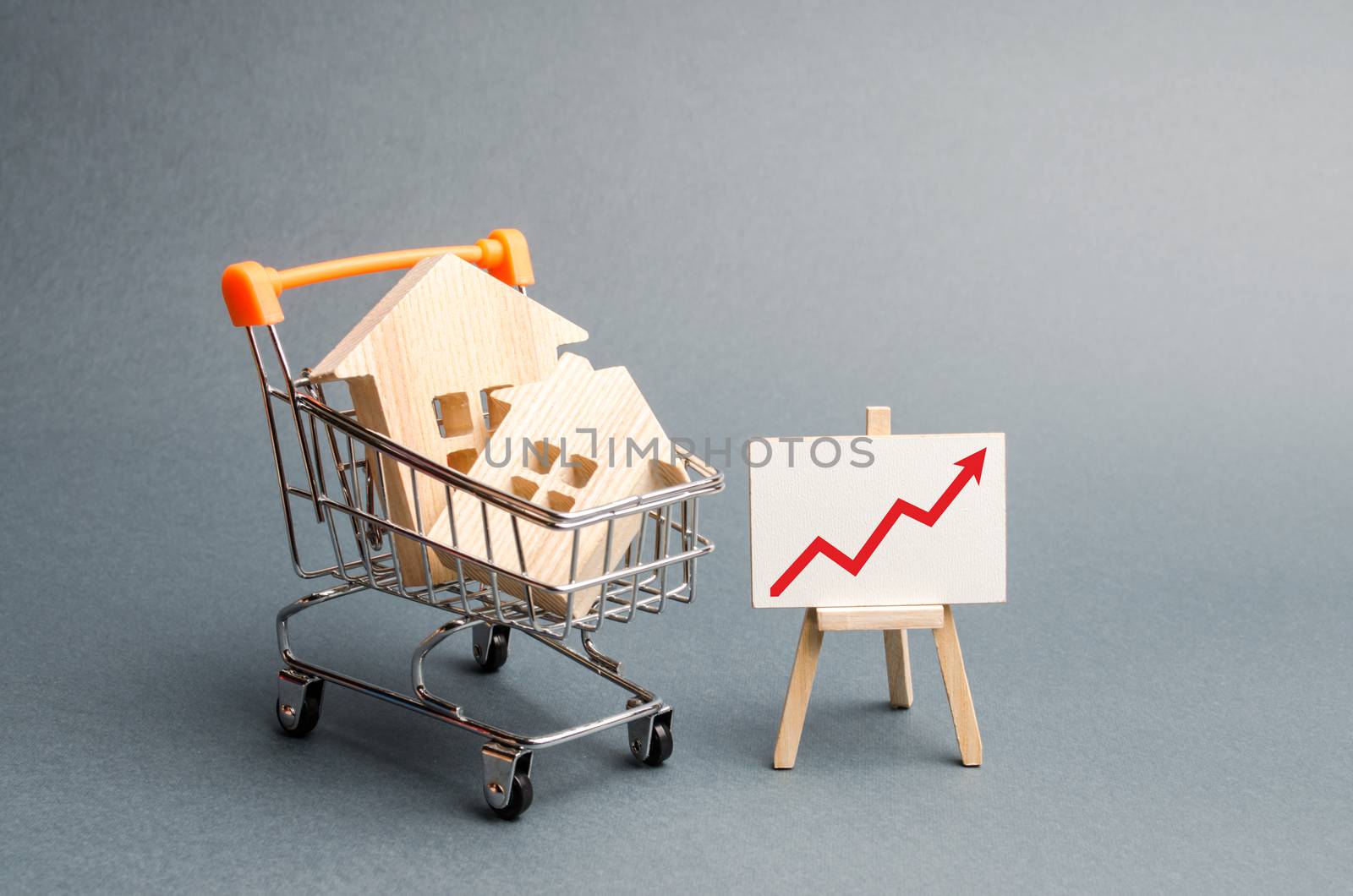 Wooden houses in a supermarket cart and red up arrow. Growing demand for housing and real estate. The growth of population. Investments. concept of rising prices for housing or rent. Selective focus